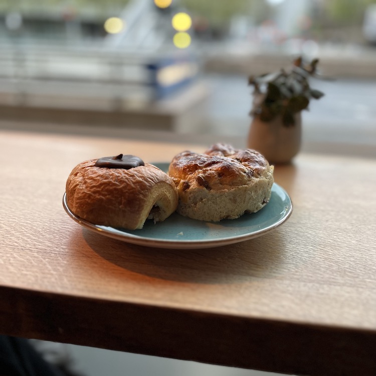 Image of two pastries (one with chocolate and marzipan, one is a currant bun) on a turquoise plate, with a blurry background.