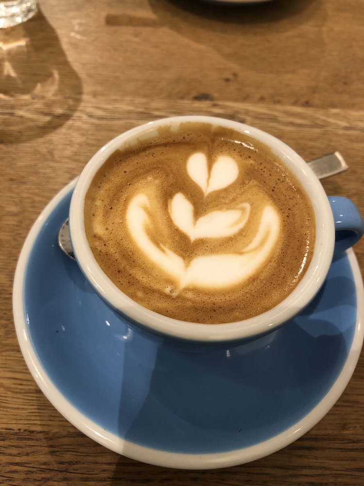 Image of a flat white with a flower latte art in a blue cappuccino cup.